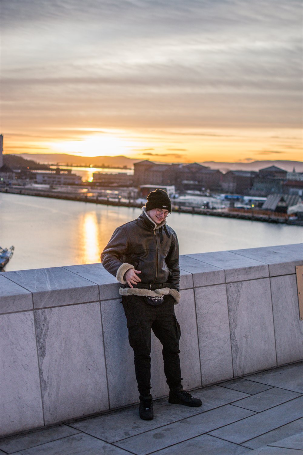 Person leaning on a wall at a harbour during sunset